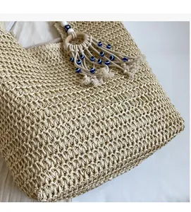 Detail of beige woven tote bag with macrame tassel and evil eye bead charms