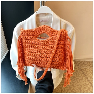 Detail of hand-woven orange tassel bag with crossbody strap on a white blazer background