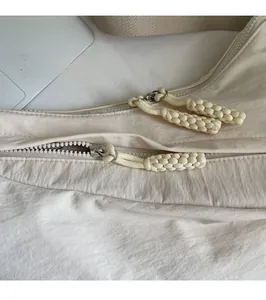 Detail of smooth double zipper with braided pullers on beige nylon crossbody bag