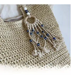 Detailed close-up of bohemian tassel pendant with Evil Eye bead on straw tote bag