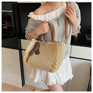 Detail of woven straw tote bag with ruffle trim and brown leather handles on shoulder