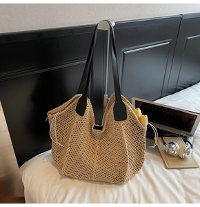 Détail d'un grand sac cabas en paille tressée avec anses en cuir noir dans un décor moderne