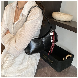 Detail of black crescent shoulder bag featuring stylish key charm and woven cord accent