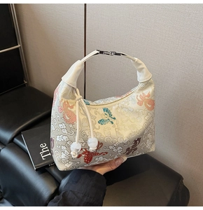Detailed embroidery of clouds and butterflies on a cream dumpling-shaped handbag