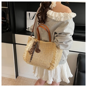 Close-up of woven straw tote bag featuring tassel trim and brown leather handles
