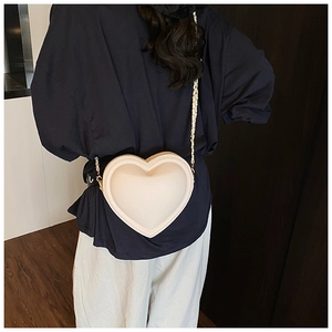 Dettaglio di una borsa a tracolla a forma di cuore crema con catena dorata su una modella