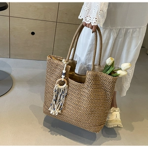 Detail of bohemian straw tote bag with woven texture and evil eye tassel charm