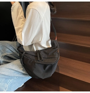 Detail of black nylon crescent bag with woven zipper pulls and orange strap accents