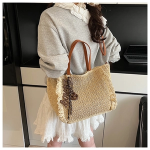 Detail of woven straw tote bag featuring ruffled edges and brown leather handles
