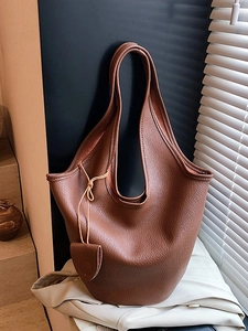 Brown lychee leather bucket handbag on beige suit jacket under natural window light