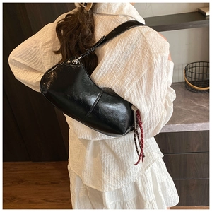 Close-up of black glossy leather crescent shoulder bag with red rope tassel charm