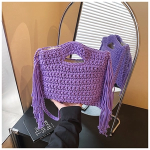 Detail of purple hand-knitted tote bag with fringe tassels and woven strap on a table
