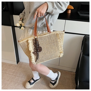 Detail of hand-woven straw tote bag featuring brown handles and stylish tassel accents