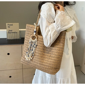 Close-up of woven straw tote bag featuring bohemian fringe and blue evil eye beads