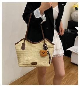 Detail of woven straw tote bag featuring brown leather straps and a plush bear charm