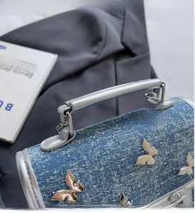 Detail of the blue denim handbag featuring a silver butterfly charm and a sleek metal handle