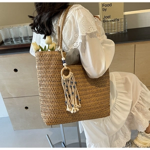 Detail of woven straw tote bag featuring bohemian tassel and evil eye bead charms