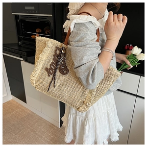 Detailed close-up of a woven straw beach tote bag with brown leather handles and fringe trim