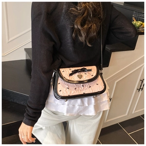 Detail of pink shoulder bag featuring black bow patterns and a heart metal pendant