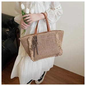 Close-up of hand-woven straw tote bag with brown leather handles and side fringe detail