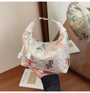 Close-up of embroidered canvas dumpling bag with goldfish patterns and jade tassel detail