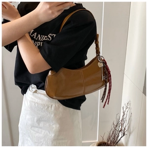 Detail of glossy caramel hobo bag with heart charm and woven tassel knot