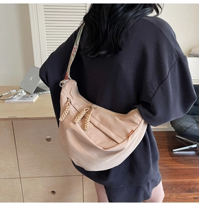Detail of beige crescent bag featuring woven zipper pulls and pattern webbing strap