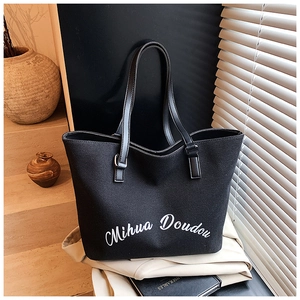 Dettaglio della borsa tote nera in tela con scritte bianche e manici in pelle alla moda