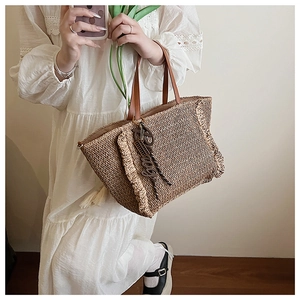 Detail of woven straw tote bag featuring brown fringe and premium leather handles