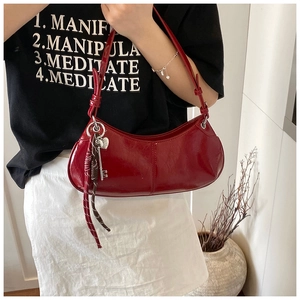 Detail of wine red patent leather crescent bag with silver heart charm on model
