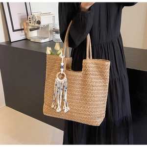 Detail of woven straw tote bag featuring bohemian tassel with evil eye charms