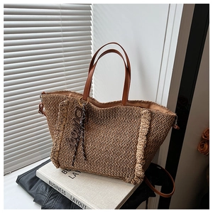Detail of woven straw tote bag with brown leather handles and wavy edge on a book