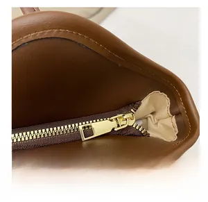 Detail view of a smooth gold metal zipper and light fabric lining on a brown leather tote