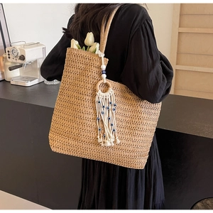 Detail of woven straw tote bag featuring white cotton tassel with blue eye element beads