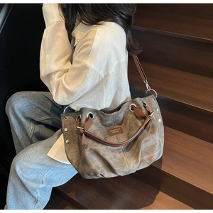 Fashionable grey canvas tote bag with brown leather handles worn by a female model