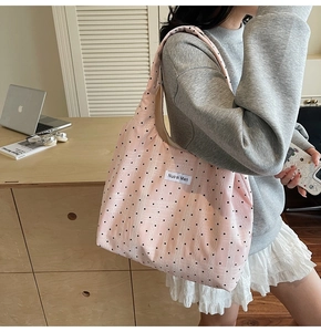 Détail d'un grand sac cabas rose à pois noirs porté à l'épaule dans un décor doux