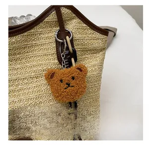 Close-up of brown plush bear charm with silver metal clasp on woven straw tote bag