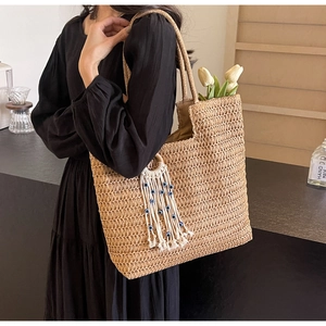 Detail of woven straw tote bag featuring a cotton tassel with a blue evil eye bead