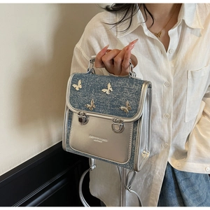 Detail of denim and silver mini bag featuring metallic butterfly charms and buckles