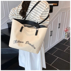 Dettaglio di una borsa tote in tela beige con manici in pelle nera e logo Mihua Doudou