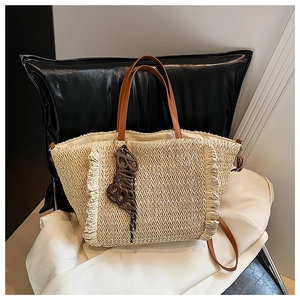 Close-up of beige woven tote bag featuring brown leather handles and fringe tassels