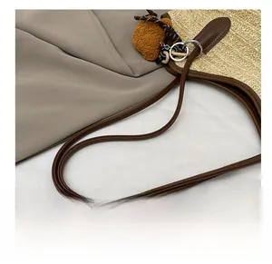 Detail of woven straw tote bag featuring brown leather shoulder straps and fuzzy pom charm