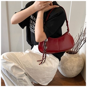 Detail of red crescent underarm bag in glossy finish with woven rope charm on shoulder
