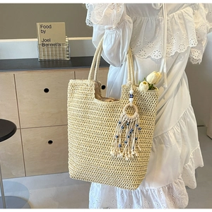Detail of handwoven beige tote bag with a blue eye tassel charm on a white dress