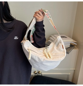 Detail of white crescent nylon crossbody bag featuring colorful floral embroidered wide strap
