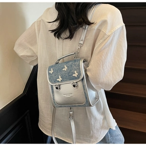 Detail of silver leather and denim backpack featuring 3D butterfly appliqués and branding