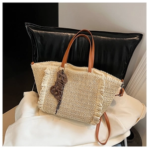 Detail of woven straw tote bag with brown leather handles and decorative fringe edges