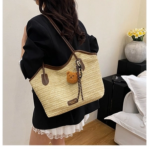Detail of woven straw tote bag featuring brown leather straps and a plush bear charm