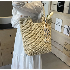 Detail view of a beige woven straw tote bag with a tassel evil eye charm and shoulder strap