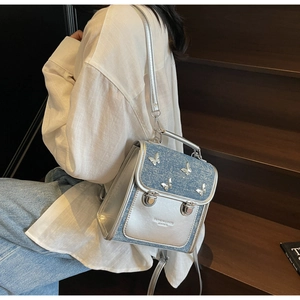 Close-up of mini silver butterfly backpack with blue denim texture and fashion text